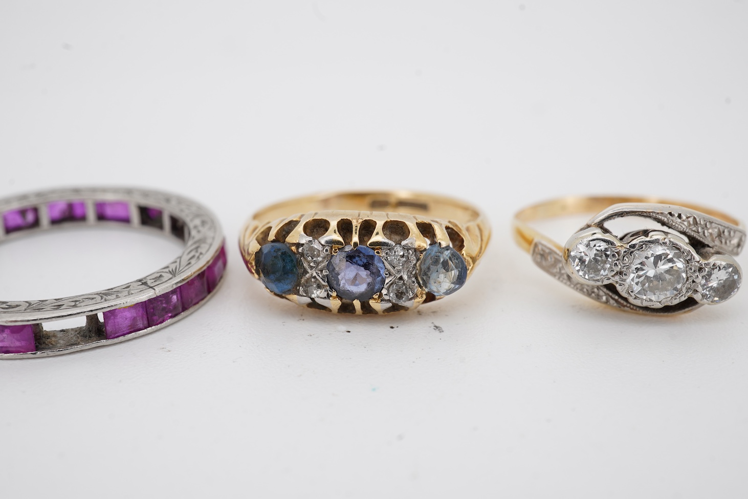 A yellow metal and illusion set three stone diamond crossover ring, size I, an 18ct, sapphire and diamond chip set ring, a modern 18ct gold and six stone sapphire set ring, with diamond chip border and an engraved white